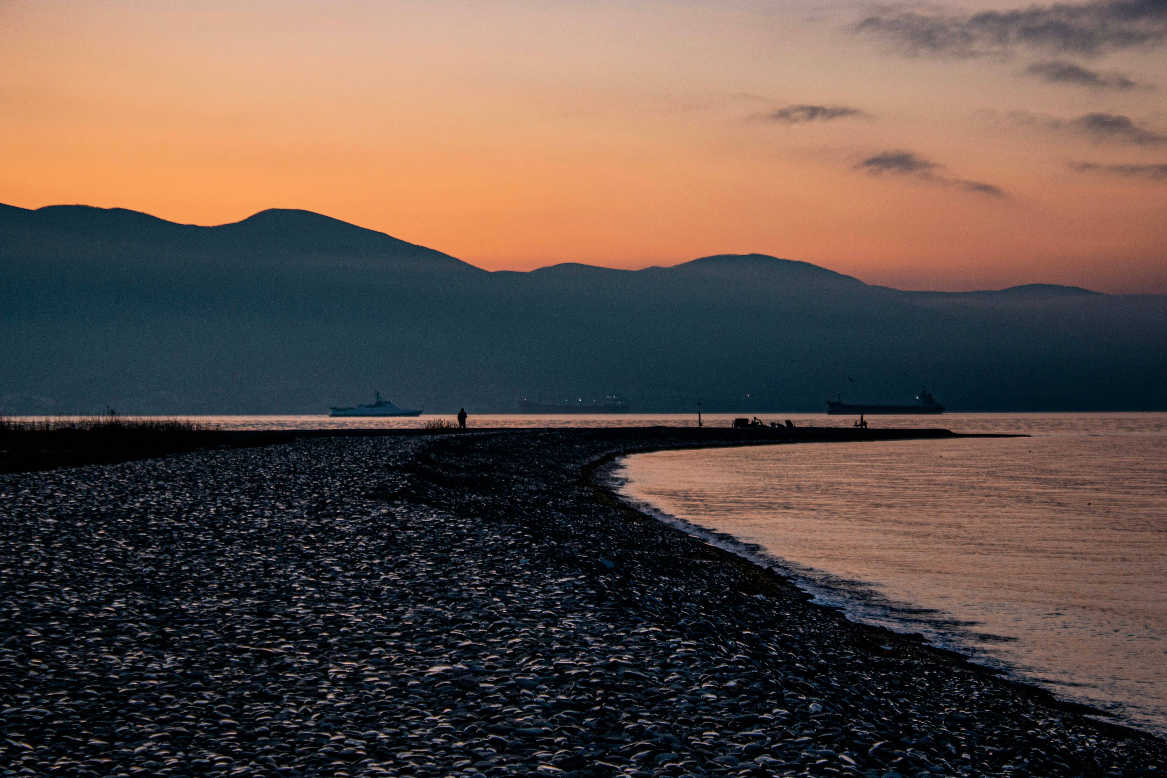 Sunset over mountains and a pebble beach.