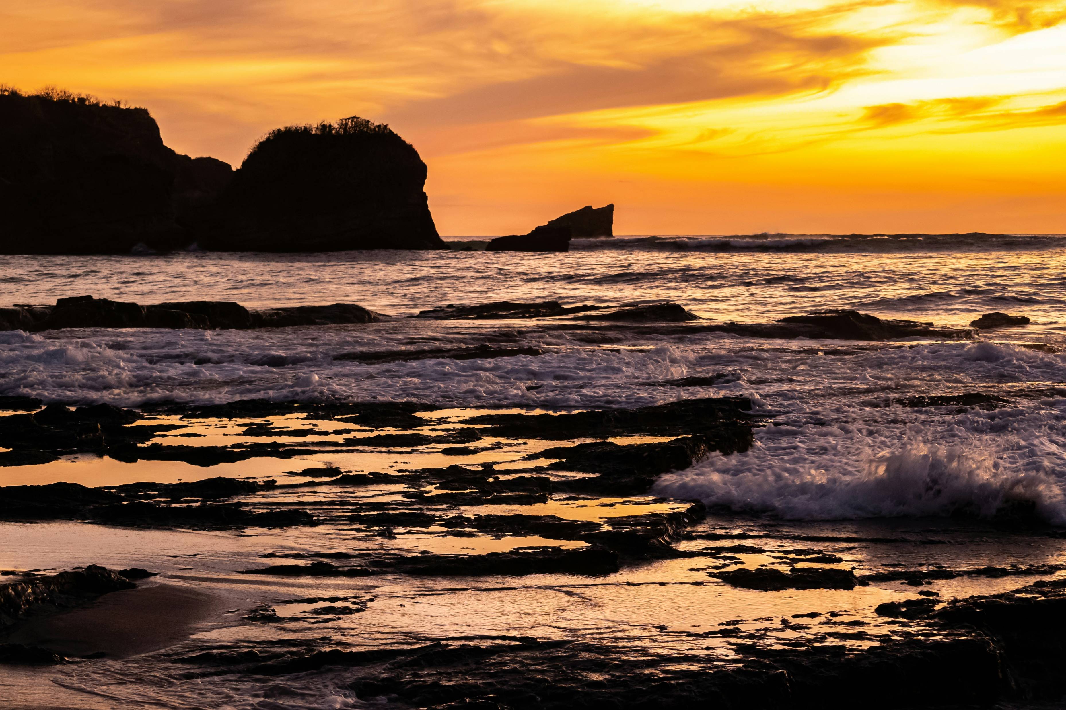 a sunset over the ocean with waves crashing on the rocks